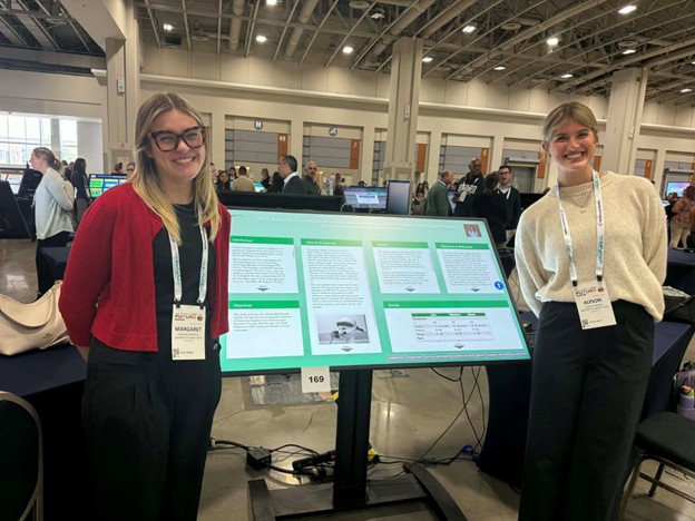 Two students standing by a research poster at a conference
