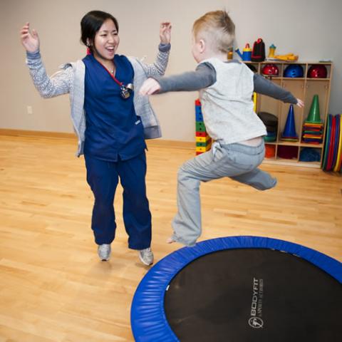 Child jumping on small trampoline with health care worker watching happily