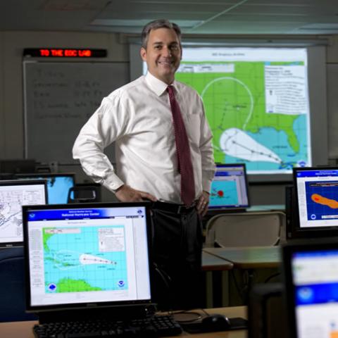 Man standing in emergency operations center surrounded by weather maps