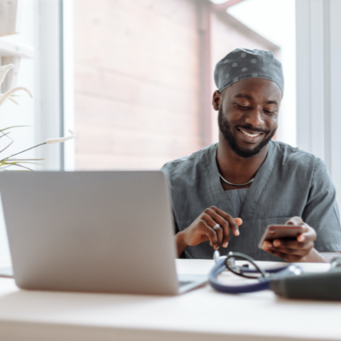 man in scrubs working on a laptop with a stethoscope next to him