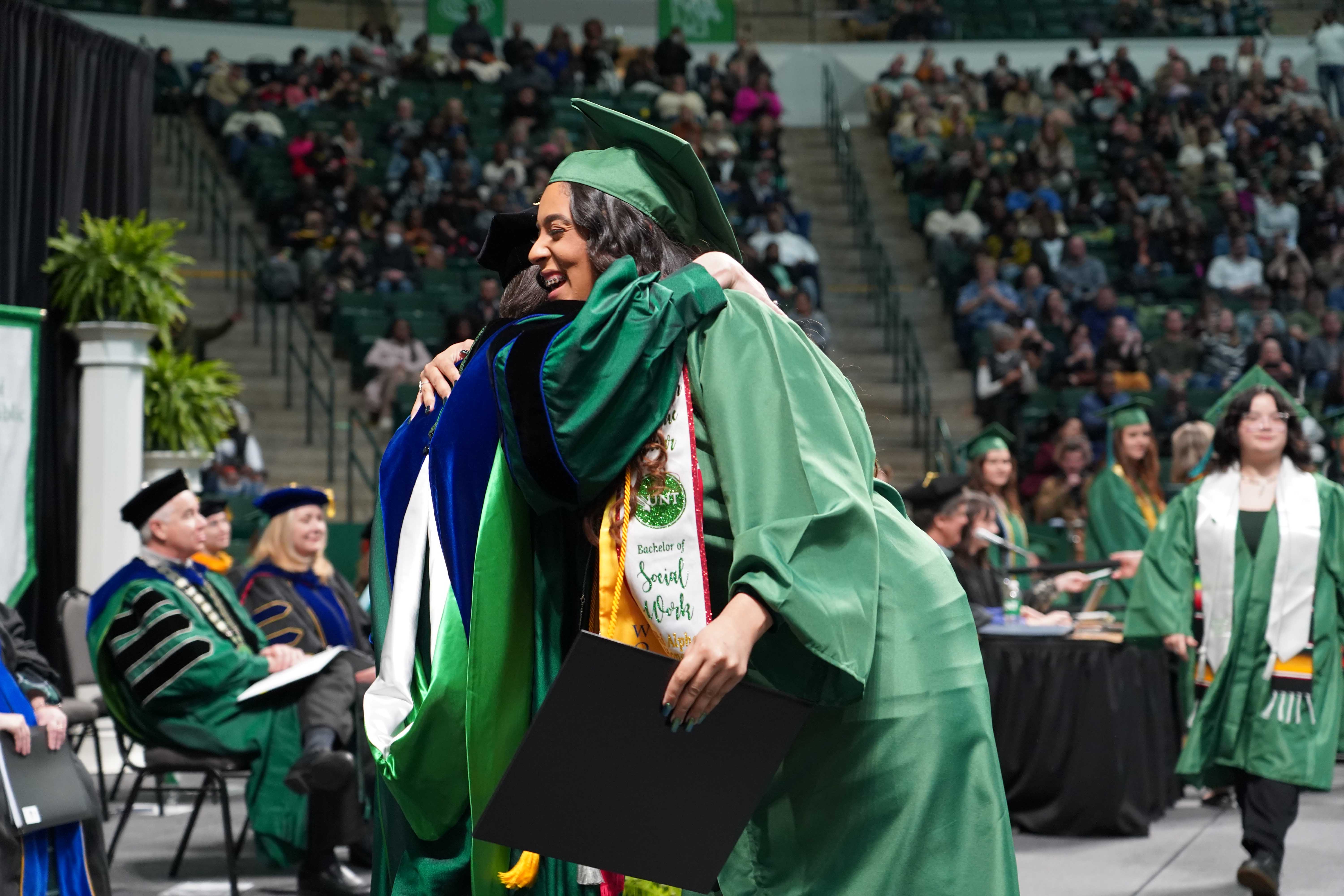 Female social work graduate hugging department chair as she walks across the stage to get her diploma