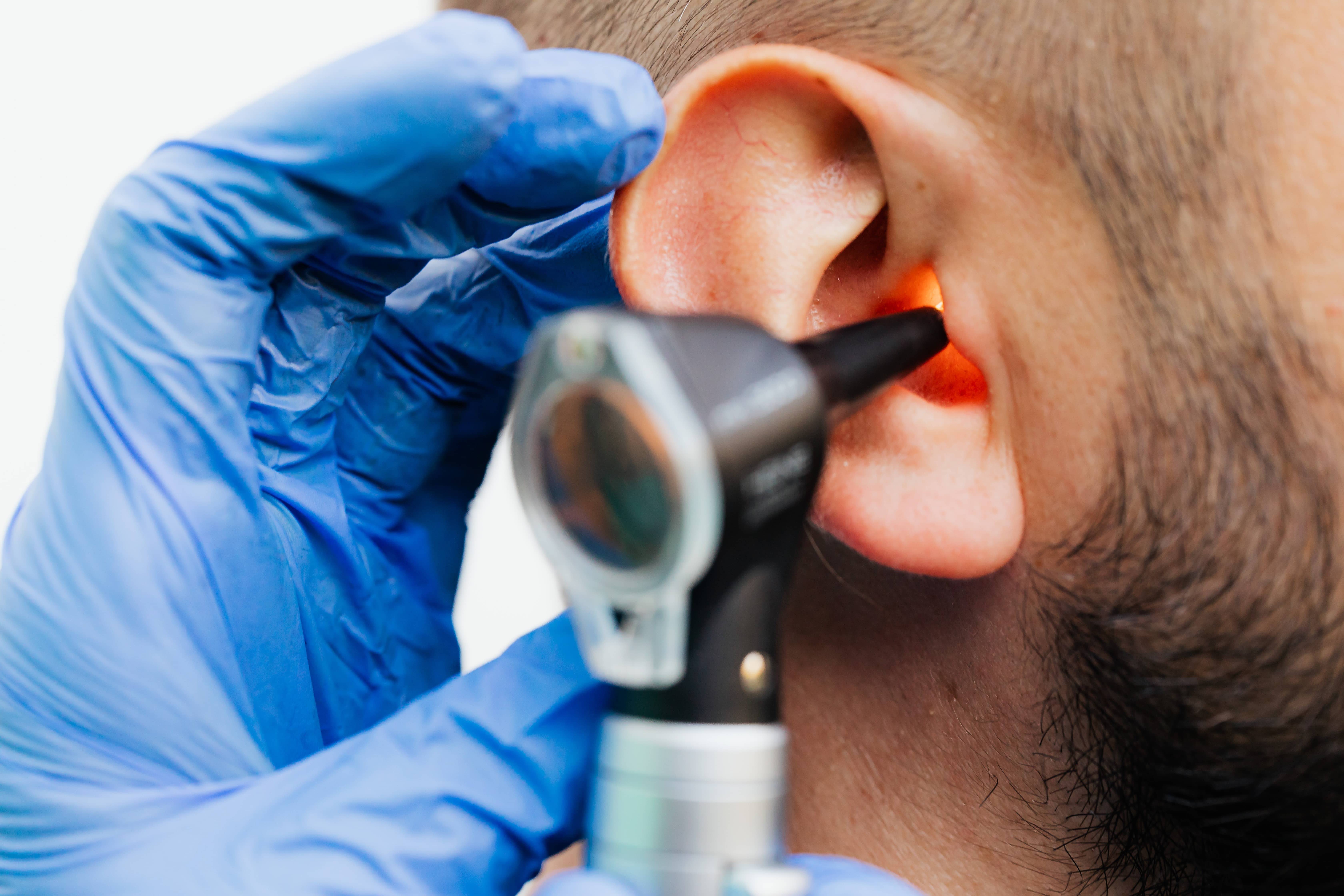 Gloved hands inserting an otoscope into a patient's ear