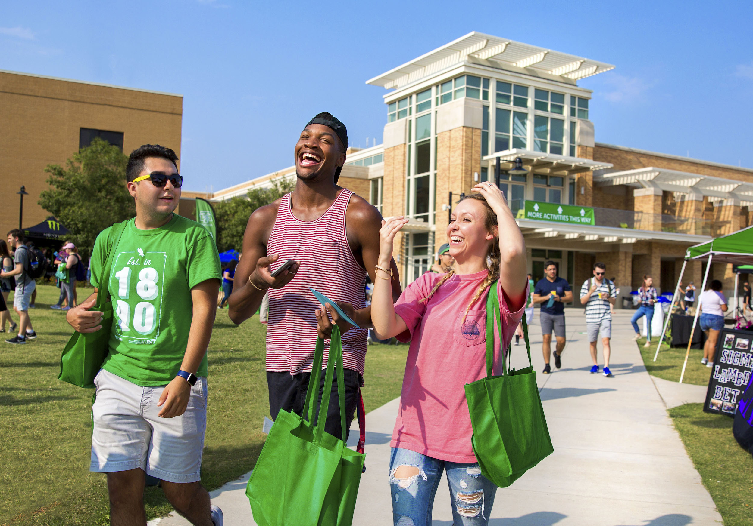 Three students - a latin male, a black male and a white female, walking outside the union with smiles on their faces